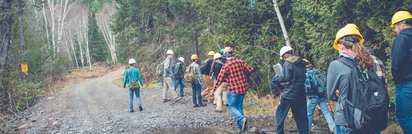 Students in a field class, wearing hardhats walking down a dirt road