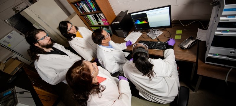 Faculty Tarun Dam with graduate students sitting around a lab computer