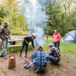 Students around a campfire with a tent in the background.