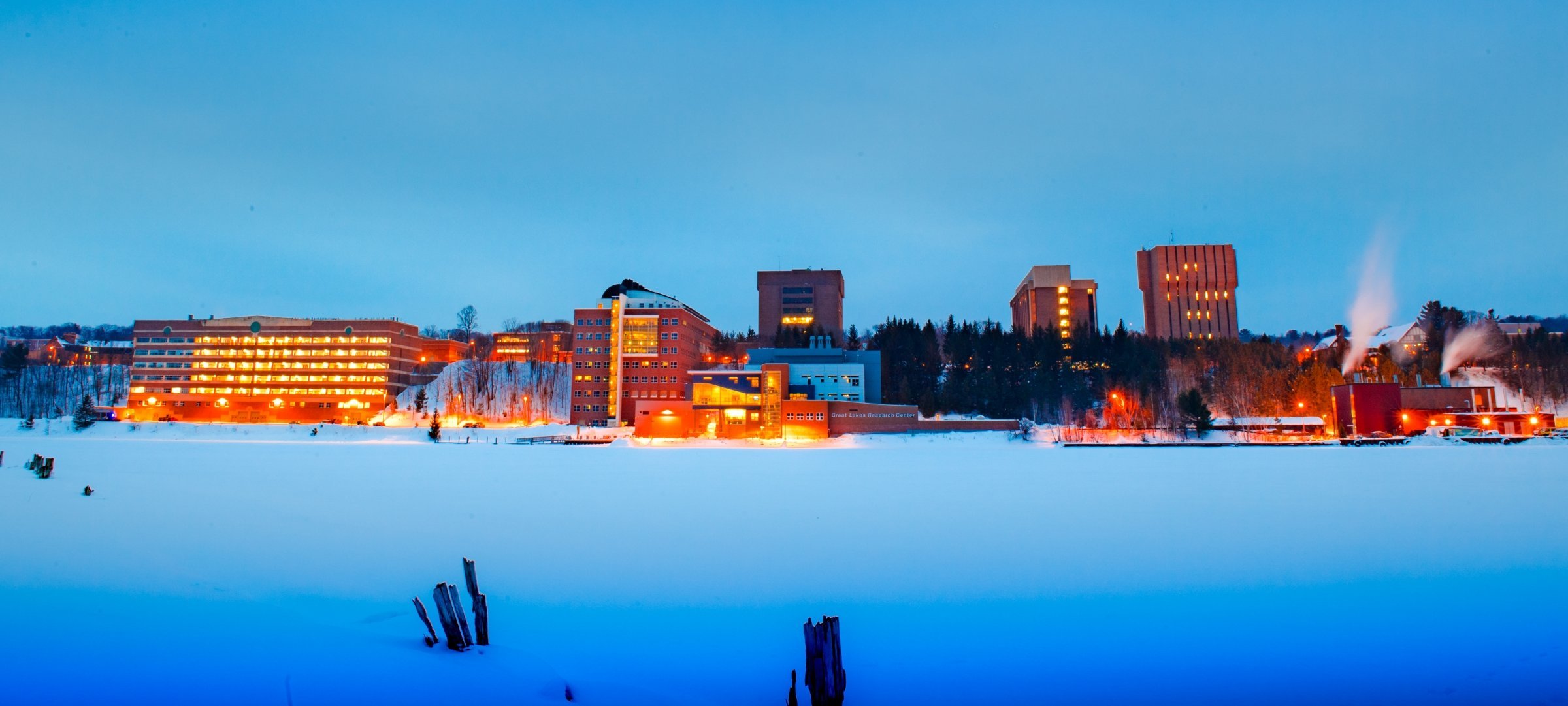 Bright, snowy campus from across the frozen water in morning light