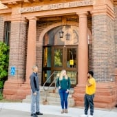 Two students and a professor stand outside the Academic Office Building.