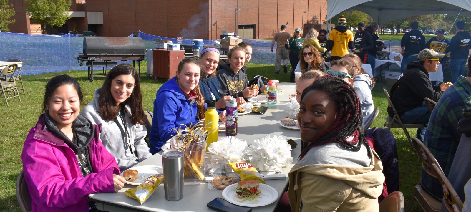 Students and family pose for the camera while sitting at tables eating.